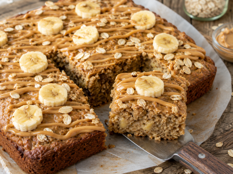 Peanut butter banana oat snack cake topped with banana slices, peanut butter drizzle, and scattered rolled oats.