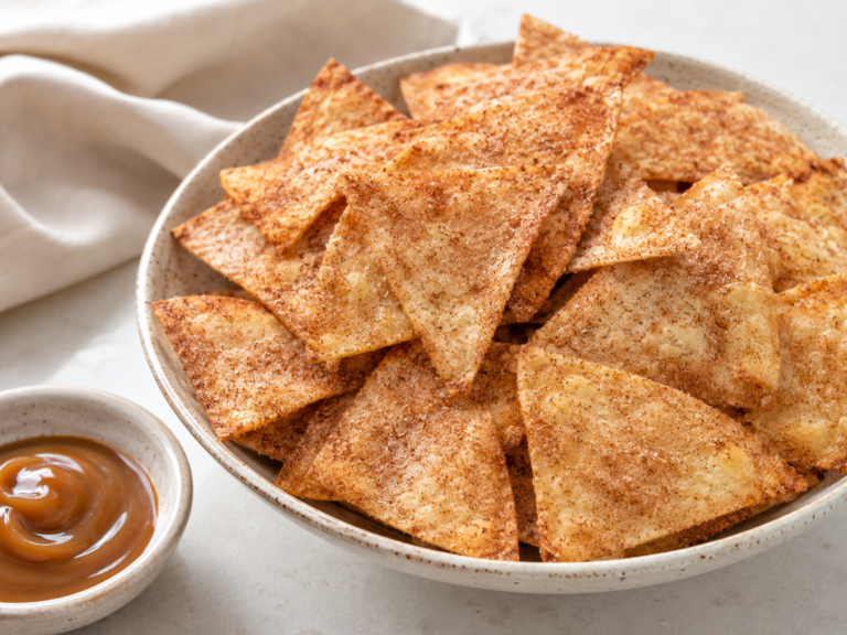 Air Fryer Cinnamon Sugar Tortilla Chips piled in a bowl with a cinnamon sugar coating and a small dish of caramel dip nearby