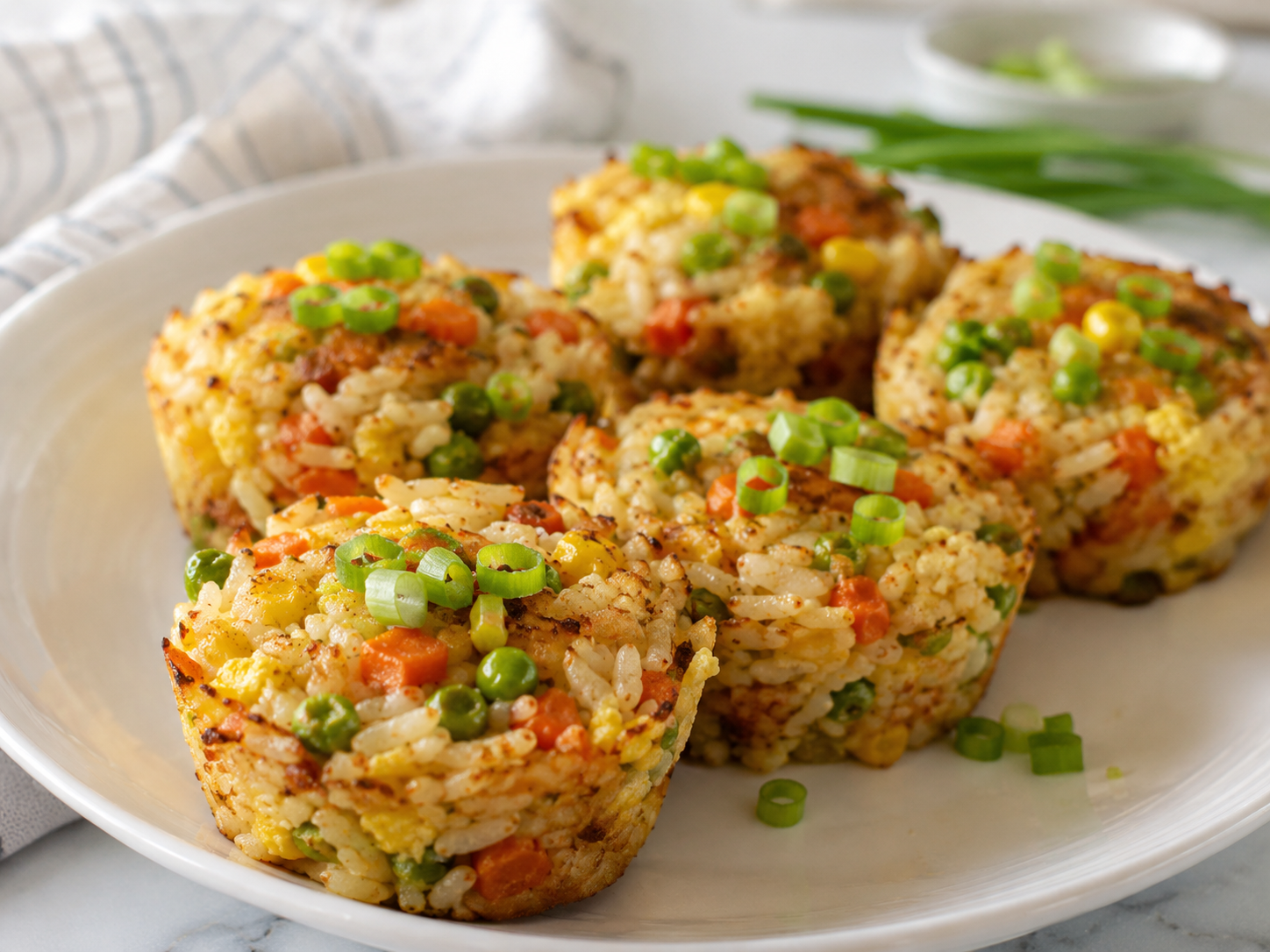 Frozen veggie fried rice muffins made with rice, peas, carrots, corn, egg, and green onions served on a white plate.